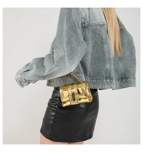Détail d'un mini sac doré effet miroir avec chaîne, porté avec veste en jean et jupe noire