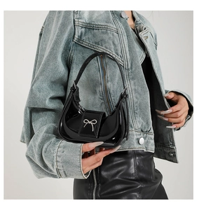 Glossy black patent leather handbag with silver metal bow detail and half-moon silhouette
