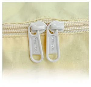 Detail of light yellow backpack showing smooth dual metal zippers with engraved logo