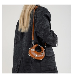 Detail of a brown glossy leather moon bag featuring metallic studs and a slim strap