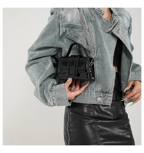 Close-up of black patent leather mini bag with silver chain strap worn by a model