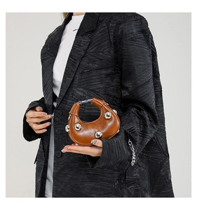 Close-up of brown crescent handbag with silver studs on a stylish textured suit jacket