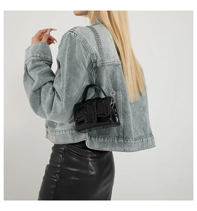 Detail view of the black patent leather mini square bag with silver chain strap on model