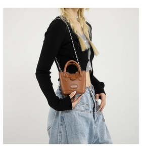 Detail der braunen Mini-Eimertasche mit Litschi-Struktur und silberner Kette für Damen