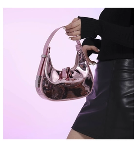 Detail view of pink mirror-finish metallic hobo bag held by a model in black outfit