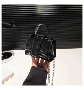 Détail du mini sac en cuir verni noir avec chaîne argentée sur surface blanche