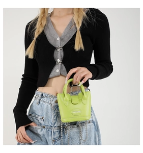 Detail der neongrünen Mini-Beuteltasche mit Metallkette, getragen von einem Modell im Casual-Look