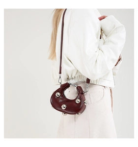 Macro shot of silver studs and glossy wine red leather on a crescent crossbody bag