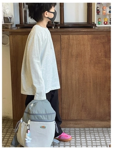 Detail of child wearing a long-sleeve sweatshirt with a gray backpack in a home setting