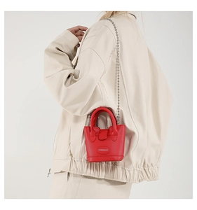 Detail der roten Mini-Beuteltasche mit Litschi-Struktur, Silberkette und Namensschild