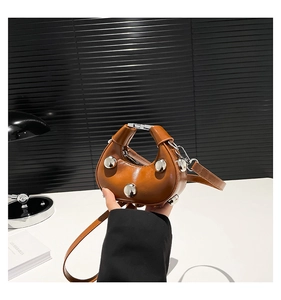Detail of a brown mini half-moon handbag featuring large silver metallic rivets and strap
