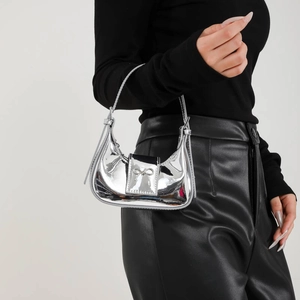 Silver glossy mini hobo bag with bow detail held by model in minimalist fashion setting