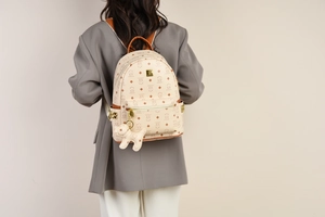 Detail eines beigen Rucksacks mit Bärenprint, braunem Leder und Hundeanhänger