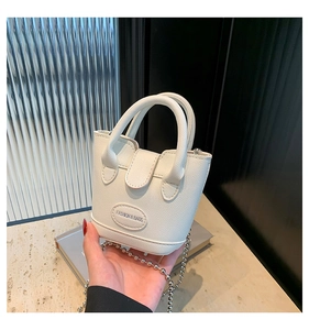 Detail der weißen Mini-Eimertasche mit silberner Kugelkette und Logo auf Steinfläche