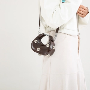 Fashionable dark brown half-moon crossbody bag with silver studs worn by a model