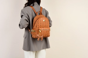 Detail eines braunen Rucksacks mit Monogramm, Nieten und süßem Welpenanhänger
