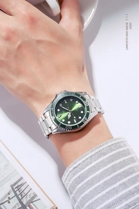 Close-up of a green dial quartz watch with luminous hands and steel strap on wrist