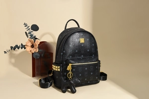 Detail eines schwarzen Lederrucksacks mit Logo-Muster und goldenen Nietendekoren