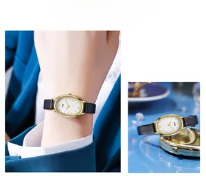 Detail view of oval gold watch with Roman numerals and slim black leather strap