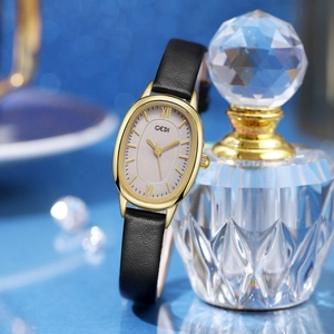 Detail of elegant oval gold watch with black leather strap near a crystal bottle