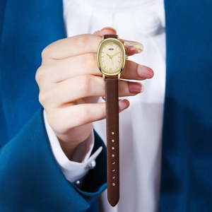 Macro detail of oval gold watch face with roman numerals and brown leather strap