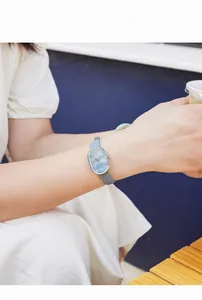 Close-up of elegant oval mother-of-pearl watch face with gray leather strap on wrist