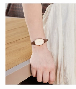Detail of oval gold case and brown leather strap watch worn on a woman's wrist