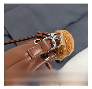 Detail of silver metal buckles and tan faux fur pom-pom on brown PU leather handbag
