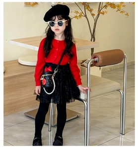 Close-up of a kids black quilted bucket bag with pearl chain and red accessories