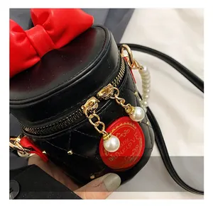 Close-up of black quilted bucket bag featuring a red bow and pearl chain details