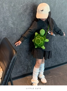 Detail of hand-crocheted turtle crossbody bag in green wool shown on a child model