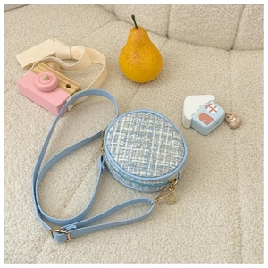 Detail of blue tweed round kids bag with gold hardware and flower pendant on plush background