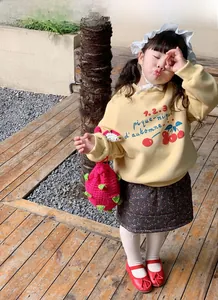 Fille en sweat jaune et jupe marron avec un sac bandoulière en forme de fruit du dragon