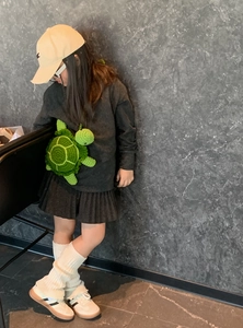 Detail of a handmade green crochet turtle crossbody bag worn by a child model outdoors