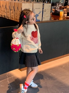 Détail d'un sac fraise en crochet fait main porté avec un pull en tricot pour enfant