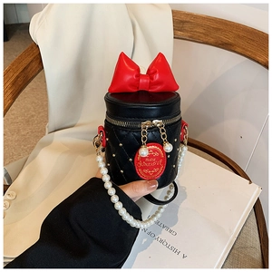 Detailed view of kids mini bucket bag with red bow, pearl chain and black quilted leather