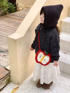 Close-up of a handmade crochet apple cross-body bag for kids paired with a winter knit outfit