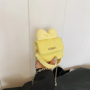 Detail of yellow tweed mini bag featuring a large bow and gold metal heart hardware