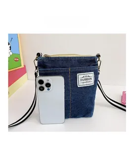Detail of blue denim crossbody bag with fashion label and striped strap next to phone