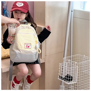 Asian child wearing yellow and grey patchwork backpack against a warm wooden background