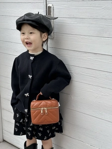 Brown quilted mini handbag with gold zippers held by child model in chic black outfit