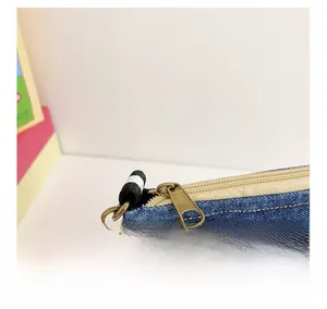 Detail of dark denim crossbody bag showing smooth metal zipper and yellow stitching