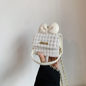 Detailed close-up of a sweet white tweed girls' bag with large leather bow and gold chain
