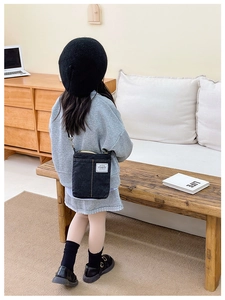 Close-up of black denim kids crossbody bag with adjustable strap and fashion label detail