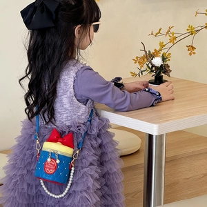 Kids quilted cylinder bag with red bow, pearl chain and blue crossbody strap on model