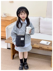 Close-up of black denim kids crossbody bag featuring white fashion label on sofa