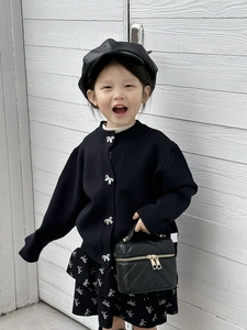 Detail view of girls' black knit cardigan with silver bow buttons and ruffled skirt