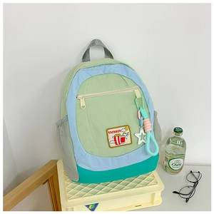 Detail of color-block kids backpack showing front zipper pocket and star charm accessory
