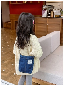 Detail of blue denim crossbody bag with fashion label and striped shoulder strap
