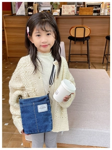 Detail of blue denim kids crossbody bag with fashion label and striped strap on model
